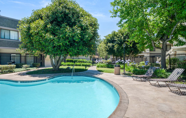 a swimming pool with chairs and trees in front of a building