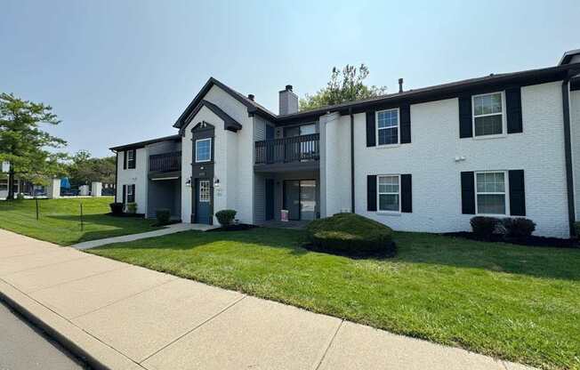 A white two-story apartment building with a black roof and a balcony on the second floor.