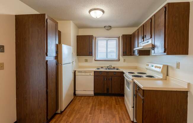 Kitchen with wooden cabinets and white appliances with a small widow above the sink at Parkwest Gardens West Fargo, ND 58078 