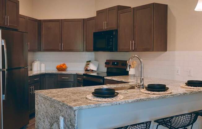 A kitchen with a granite countertop and black chairs.