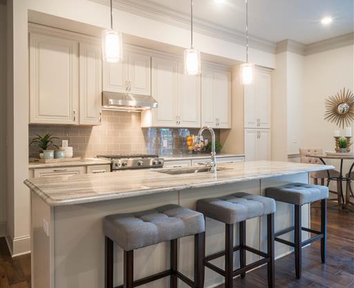 A modern kitchen with white cabinets, pendant lights, and a large island with seating.