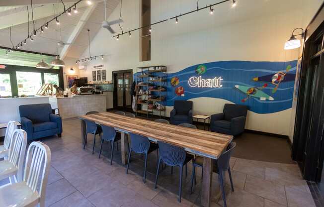 a dining area with a long wooden table with blue chairs and a large mural on the wall