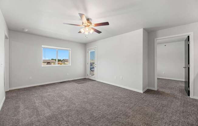 A spacious room with a ceiling fan and a window overlooking a residential area.
