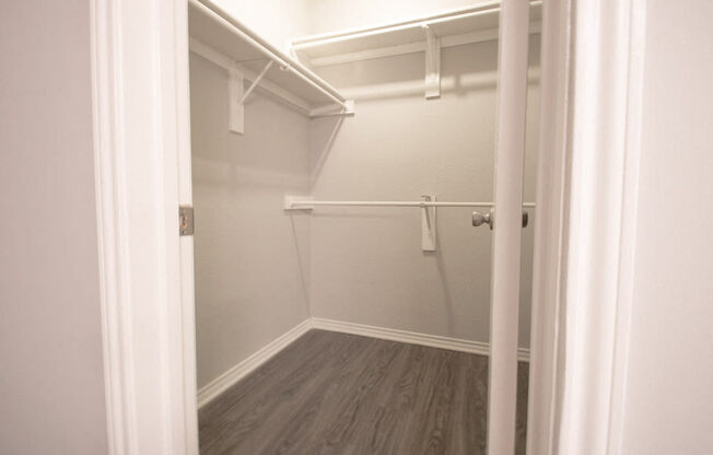 a walk in closet in a home with white walls and a wood floor at The Broadwater at Salado Creek, San Antonio