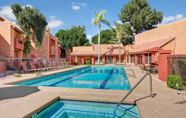 A vibrant resort-style pool here at Aspire Pinnacle Park featuring a sparkling lap pool with clear blue water, built-in lane markers, and surrounding lounge chairs for relaxing in the sun. Terracotta-toned buildings, palm trees, shaded seating areas, and landscaped courtyards create a warm, inviting setting perfect for swimming and unwinding outdoors.