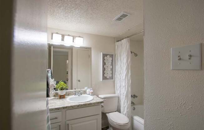 A bathroom with a white vanity in a 515 square foot 1 bedroom, 1 bath apartment home at Canyon Creek Apartments in Dallas Midtown neighborhood of Dallas, TX.