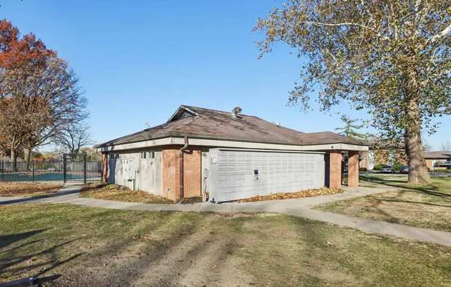 A small building with a grey roof is surrounded by a grassy area and trees.