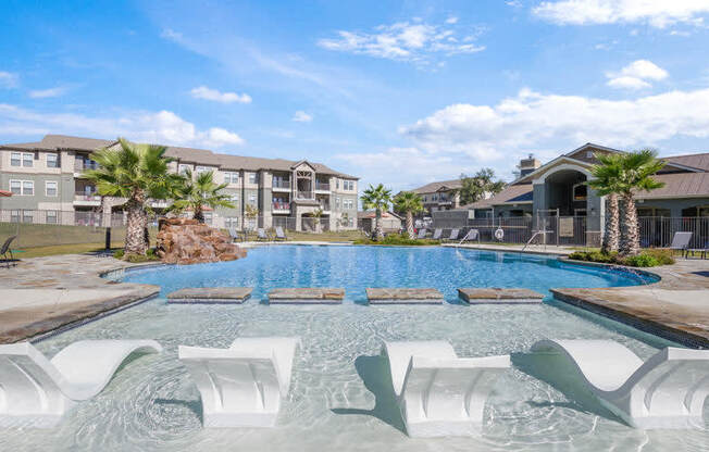 a large swimming pool with white chairs in front of an apartment building