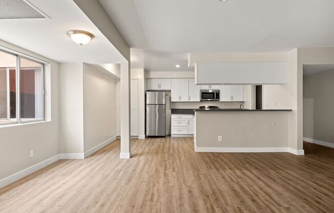 an empty living room with a kitchen in the background