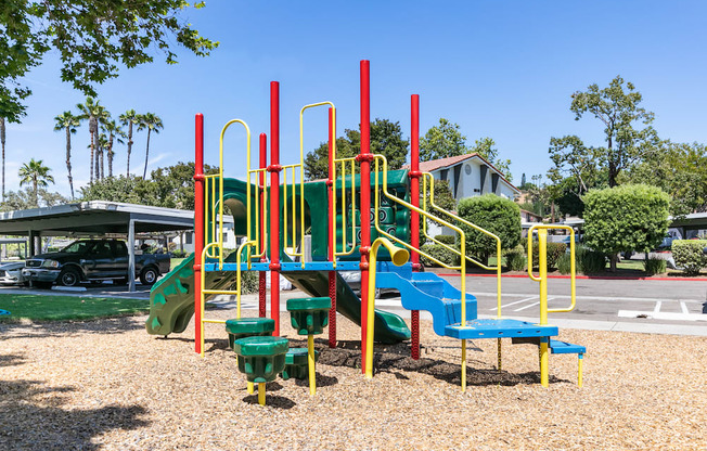 a colorful playground in a park with a parking lot in the background