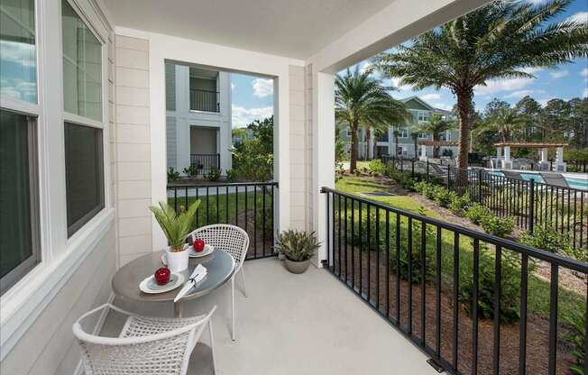 A balcony with a table and chairs overlooking a pool and palm trees.