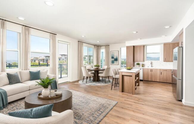 Open kitchen and living area with wood grain cabinetry, sleek surfaces, and expansive corner windows bringing in daylight and framing rolling hillside scenery.