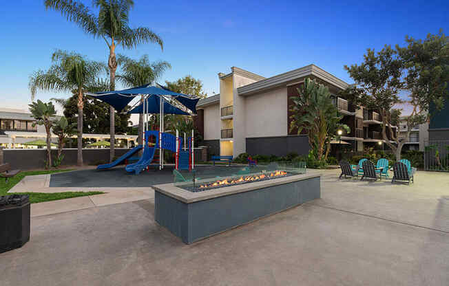 Community Fire Pit Area with Lounge Furniture and View of Playground at Madison Park Apartments located in Anaheim, CA.