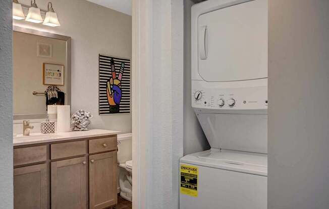 A washing machine is in a small bathroom with a mirror, toilet, and sink.