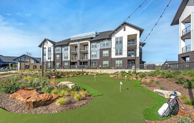 A golf hole is in the front yard of apartment buildings.