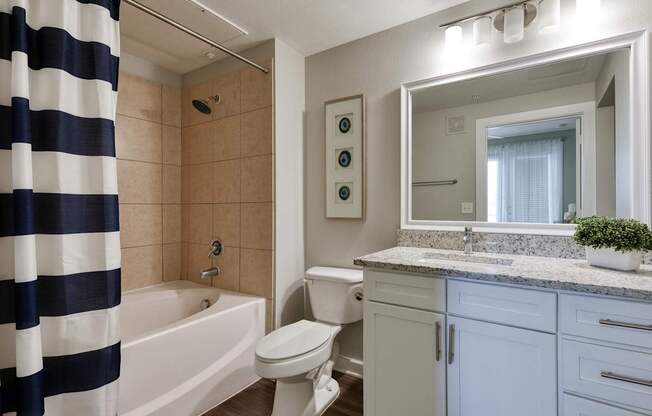 A bathroom with a white toilet, a white sink, and a white bathtub with a blue and white striped shower curtain.