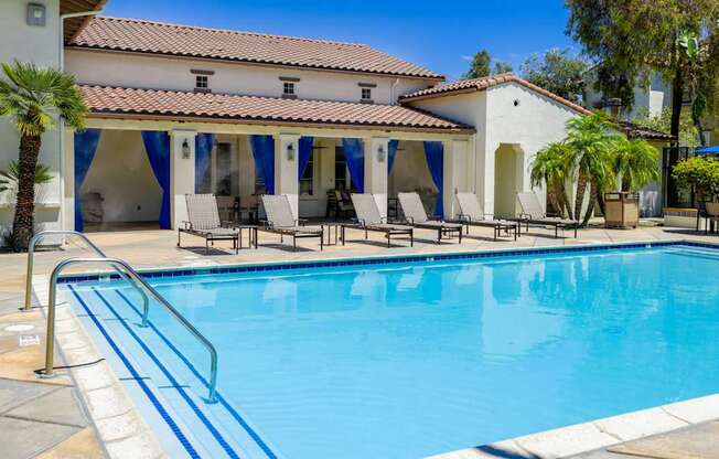 A pool with a blue tiled edge and a white building with a red tile roof in the background.