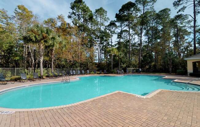 A swimming pool surrounded by trees and a brick patio.
