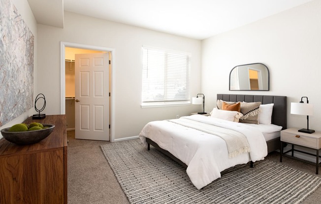 A bedroom with a large bed, a wooden dresser, and a bowl of fruit on the dresser.