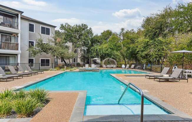 A swimming pool surrounded by lounge chairs and trees.