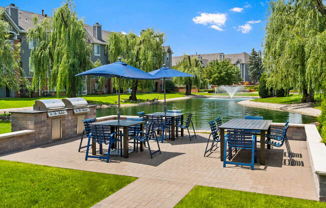 a patio with tables and chairs and umbrellas next to a pond