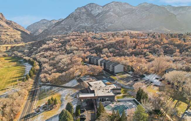 A large building sits in the middle of a forested area with mountains in the background.