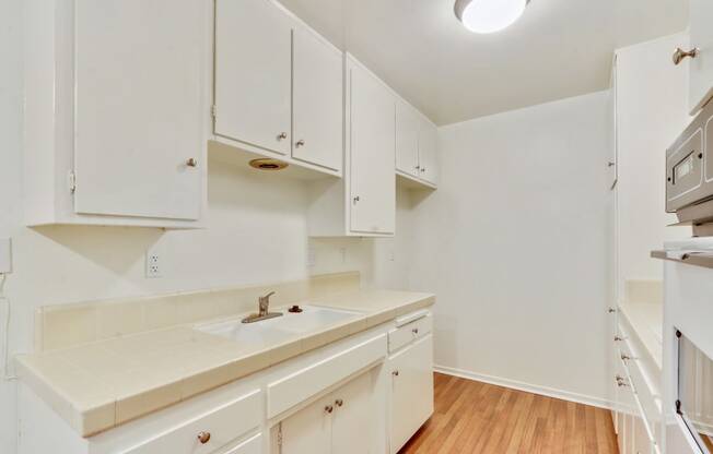 Kitchen with White kitchen cabinets and cupboards, Double white kitchen sink and Tile countertops on the right side, White Oven on the left side