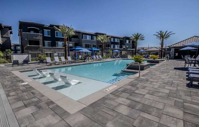 A swimming pool surrounded by lounge chairs and umbrellas in front of a building.