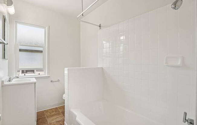 A white bathroom with a tub, sink, and window.