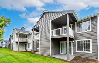 the view of a gray house with a balcony and a yard