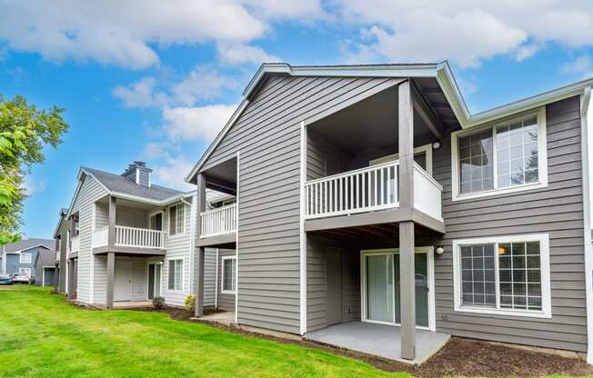 the view of a gray house with a balcony and a yard