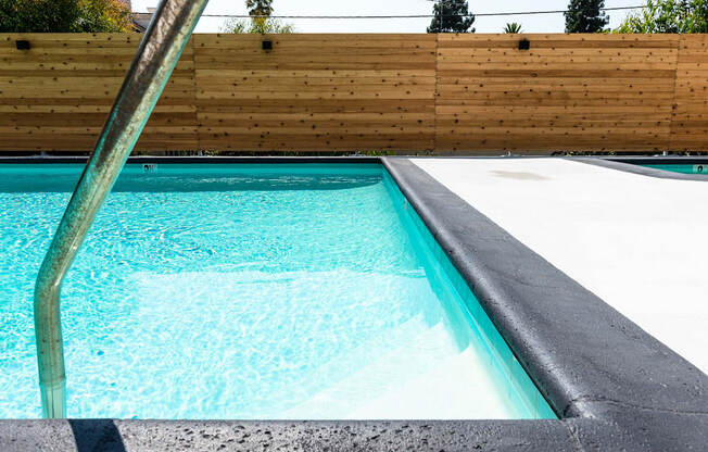 a swimming pool with a concrete coping and a wooden fence