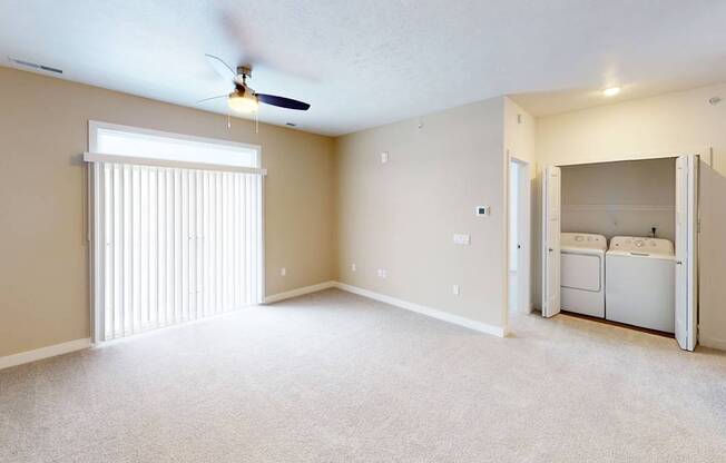 A living room with a ceiling fan and a closet with a washer and dryer inside at Meadowbrooke Apartment Homes in Kentwood, MI 49512