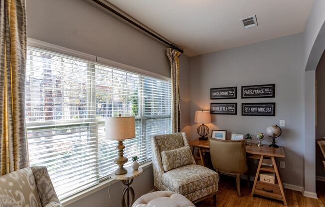 a living room with a large window and a desk with chairs