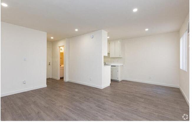 a living room and kitchen with white walls and wood floors