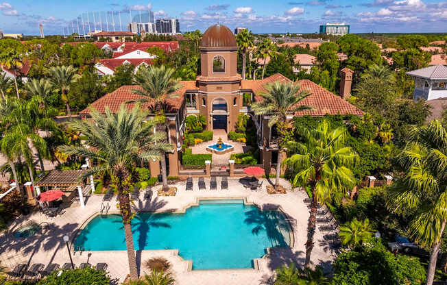 Aerial view of Mediterranean-style clubhouse with pool, palm trees, and courtyard fountain