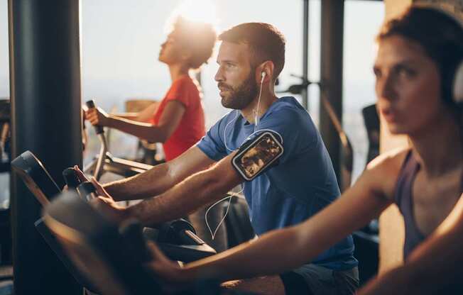 Three people are working out on exercise bikes in a gym.