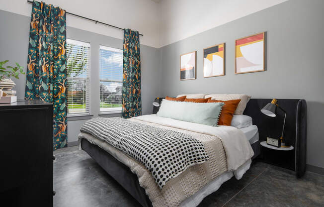 a bedroom with gray walls and a black and white bed with orange and black pillows