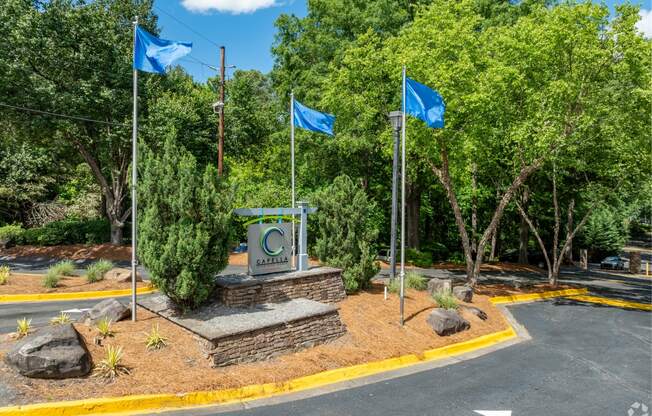 a monument with three blue flags and a road and trees