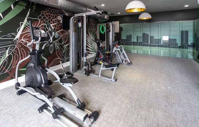 a gym with cardio equipment and a mural of a city on the wall