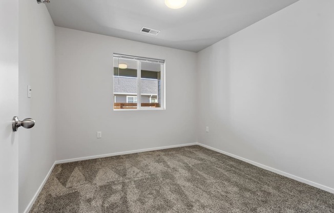 A room with a carpeted floor and a window showing a view of a building.
