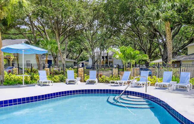 A pool surrounded by trees and chairs.