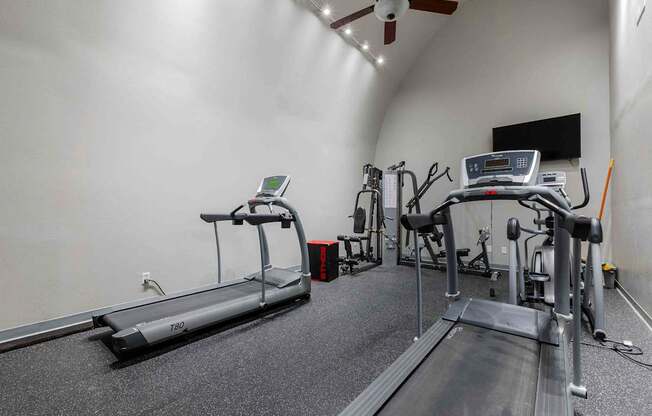 A treadmill and a rowing machine are in a well lit gym.