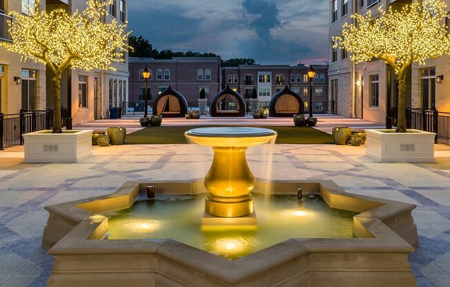 A fountain in the middle of a plaza surrounded by trees and buildings.