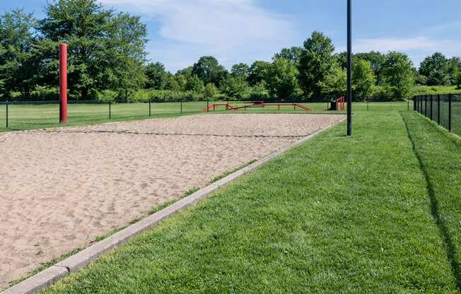 A red pole stands in a sandy area next to a green grassy area.