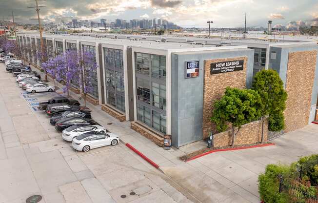 A parking lot with a white car parked in front of a building that has a sign that says "Now Leasing".