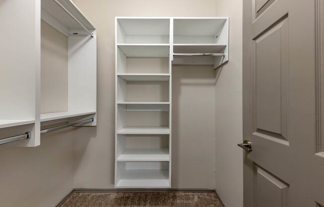 a walk in closet with white shelves and