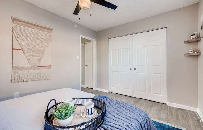 A bedroom with a bed, a ceiling fan, and a tray with a plant and two cups on it at Mountain Vista Apartments, Lakewood, 80228