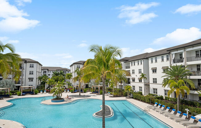 a large swimming pool with palm trees in front of apartment buildings