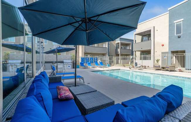 a pool area with blue couches and umbrellas at Loma Villas Apartments, California, 92408